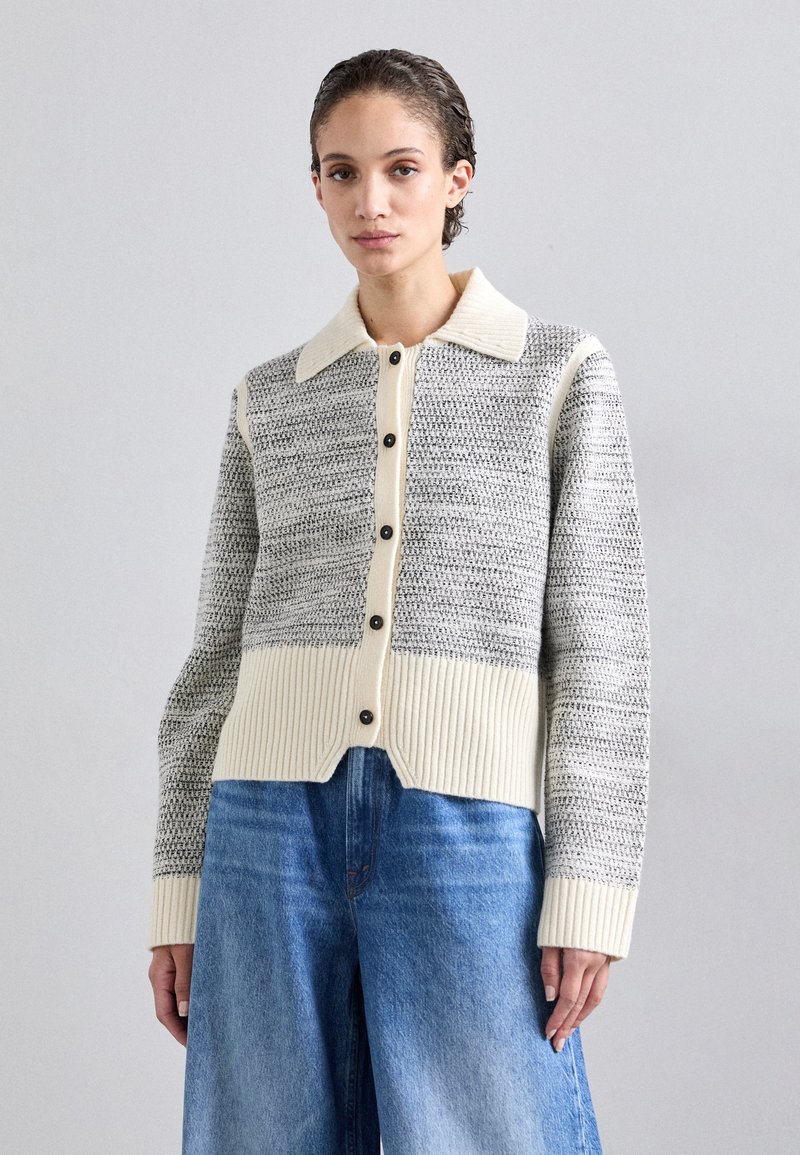 Strikket cardigan med et grå- og hvidmønstret design, cremefarvet krave, sorte knapper og ribbet kant. Lange ærmer og cropped pasform.