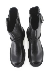 Botas de cuero negras hasta el tobillo con una textura suave, tacón bajo y cremalleras en los laterales, presentando una hebilla decorativa en la parte externa de la caña.