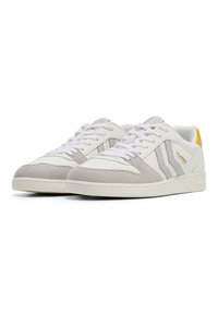 White sneakers with gray suede accents, three gray stripes, round toe, flat rubber sole, and a yellow heel tab. Laced closure.