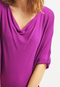 Lila draperad topp med korta ärmar, med en cowl-krage. Tillverkad av mjukt tyg med en slät textur och avslappnad passform.