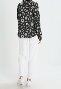 Camicia nera a maniche lunghe con motivo floreale bianco, abbinata a pantaloni bianchi a gamba larga e sneakers bianche, vista da dietro.