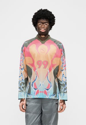 Young person with vitiligo wearing a colorful long-sleeve sports jersey with number 99 and gray shorts, standing against a plain background.