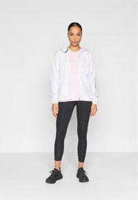 Geacă albă ușoară cu glugă, top roz cu mâneci scurte, colanți negri și pantofi sport negri. Textură netedă, design ajustat.