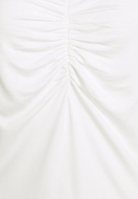 Bílá nařasená tkanina s hladkým povrchem, s vertikálními sbíranými švy, které vytvářejí jemný drapovaný efekt.