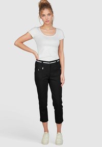 Zwarte cropped broeken met voorzakken met rits, textielstructuur, contrasterende tailleband en opgerolde zoom. Gecombineerd met een aansluitend wit T-shirt.