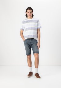 Camiseta de manga corta a rayas en azul claro y gris, combinada con pantalones cortos de denim hasta la rodilla. Los accesorios incluyen un cinturón marrón y zapatos casuales.