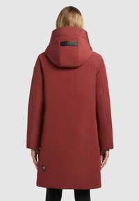 Parka isolée rouge avec une grande capuche, texture lisse et mate, et détail de logo au dos. Dispose de manches longues et d'une coupe droite.