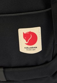 Ορθογώνιο μπεζ έμπλαστρο σε μαύρο ύφασμα με κόκκινο λογότυπο αλεπούς και το κείμενο «Fjällräven Sweden 1960» κεντημένα σε σακίδιο πλάτης.