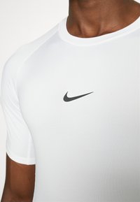 Camiseta deportiva blanca de manga corta, ajustada, con un discreto logo negro de Nike en el pecho. Tela suave, ligera y elástica.