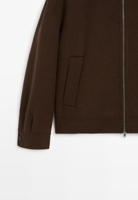 Brun uldblandingsjakke med lynlås, sidelommer og knappelukning ved manchetten, med en glat tekstur og struktureret design.
