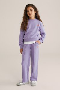 Sweatshirt aus Lavendel-Jersey und passende Hose mit orangem Logodetail. Die Hose hat zwei seitliche Taschen und einen lockeren Schnitt. Silberne Sneakers.