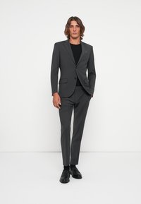 Gray suit with a slim fit design, single-button closure, and two side pockets. Paired with a black shirt and black loafers.