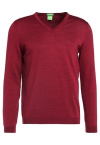 Röd v-ringad tröja i stickad tyg med långa ärmar. Har en diskret logotyp på vänster bröst och ribbade muddarna och nederdelen.