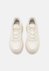 Weiße synthetische Sneaker mit strukturiertem Finish, gepolstertem Schaft und Schnürsenkeln. Besitzt goldene Logo-Akzente und eine dicke Gummisohle.