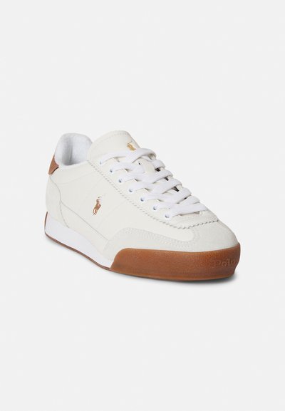 Pantofi sport albi din piele întoarsă, cu talpă de cauciuc maro, șireturi albe și un mic logo auriu pe lateral. Design cu vârf rotund.