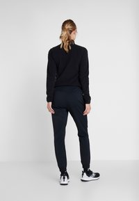 Black long-sleeve top paired with navy joggers. Joggers feature elastic cuffs; model wears black and white sneakers. Minimalist design, no patterns.