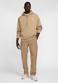 Κρεμ φούτερ με μπροστινή τσέπη και λευκό λογότυπο, συνδυασμένο με ταιριαστά κρεμ παντελόνια, κατασκευασμένα από μαλακό ύφασμα, ολοκληρωμένο με λευκά αθλητικά παπούτσια.