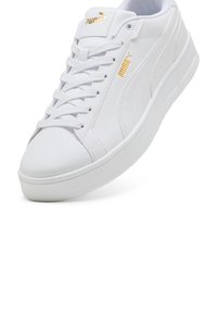 White leather sneakers with a smooth texture, featuring gold accents, a lace-up design, and a thick white sole. Subtle branding on the side.