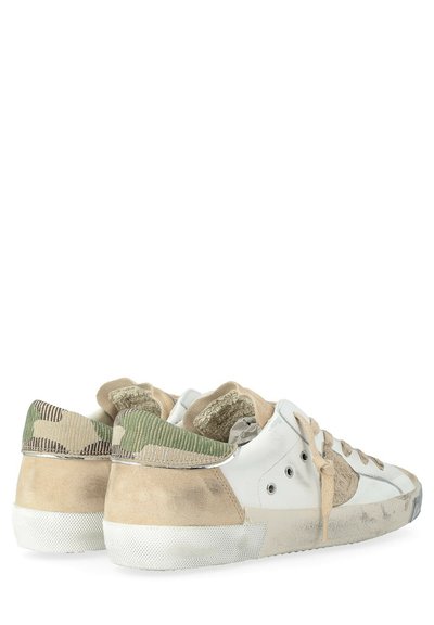 Une paire de baskets blanches usées avec des détails en suède beige et en tissu camouflage vert, des lacets visibles et des semelles en caoutchouc roussi, sur un fond blanc.