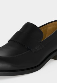 Μαύρο δερμάτινο loafer τύπου slip-on με χαμηλό τακούνι και φαρδιά λωρίδα στην κορυφή, με διακριτικό ανάγλυφο λογότυπο στη λωρίδα.
