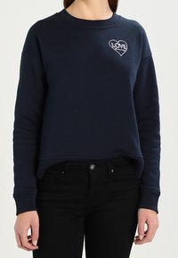 Sudadera de color azul marino con mangas largas, cuello redondeado y dobladillo corto; presenta un corazón blanco con "LOVE" bordado en el pecho.