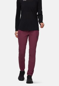 Bordeauxkleurige wandelbroek van elastische stof, aansluitend ontwerp, met zijzakken en logo-detail. Gecombineerd met een zwart T-shirt met lange mouwen en zwarte schoenen.