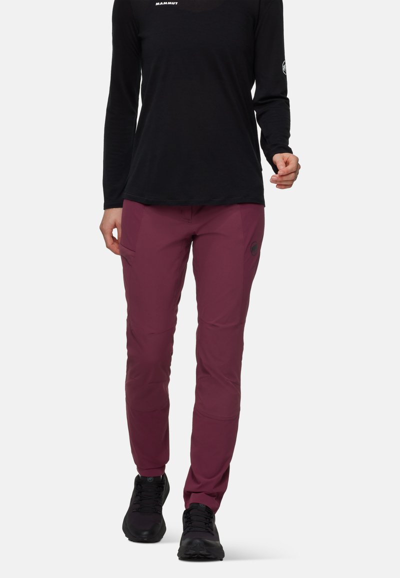 Bordeauxkleurige wandelbroek van elastische stof, aansluitend ontwerp, met zijzakken en logo-detail. Gecombineerd met een zwart T-shirt met lange mouwen en zwarte schoenen.