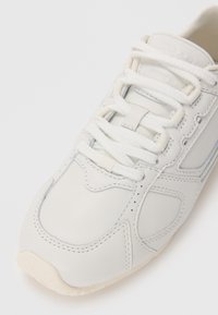 Světlé šedé kožené tenisky s hladkým povrchem, bílými tkaničkami a jemnými prošívanými detaily. Zaoblená špička a gumová podrážka.