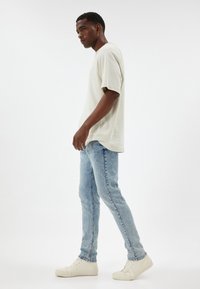 T-shirt rilassato beige chiaro, con maniche corte, abbinato a jeans slim-fit blu chiaro e sneaker bianche. Design semplice e trama del tessuto casual.