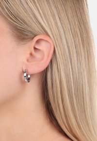 Orecchino a cerchio in argento con una finitura lucida, caratterizzato da un design circolare e senza soluzione di continuità che abbraccia strettamente l'orecchio.