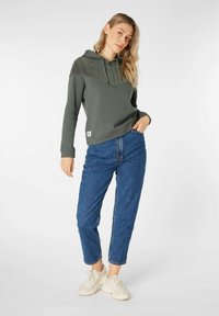 Groene hoodie met een textuurpaneel, blauwe jeans en lichte sneakers. De hoodie heeft een trekkoord en een buidelzak aan de voorkant.