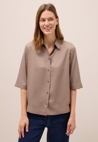 Kortärmad, taupe knapp-up blus gjord av mjukt tyg med krage och lätt lyster, i kombination med mörkblå jeans.