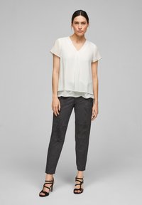Blusa bianca leggera con scollo a V e maniche corte, design a strati. Abbinata a pantaloni attillati grigio scuro con texture e sandali neri.