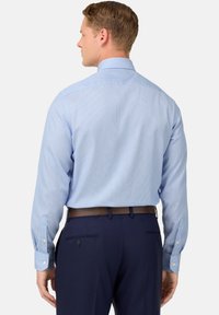 Gaiši zils svītrains krekliņš ar garām piedurknēm un pogu aprocēm, ar klasisku apkakli un gludu tekstūru. Valkāts kopā ar tumšiem biksēm.