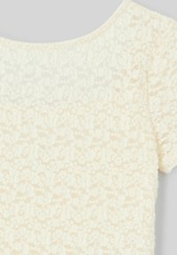 Top à manches courtes en dentelle crème texturée avec un motif floral, présentant un large col rond et un aspect doux et délicat.