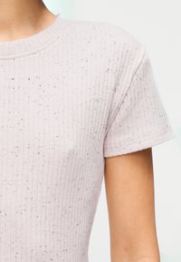 Ροζ ριμπ κοντομάνικο μπλουζάκι με στρογγυλή λαιμόκοψη και υφή με μικρές μαύρες κηλίδες διάσπαρτες σε όλη την επιφάνεια.