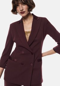 Blazer bordeaux doppiopetto con dettagli in satin, rever a scollatura e due tasche frontali. Tessuto morbido e maniche a tre quarti.