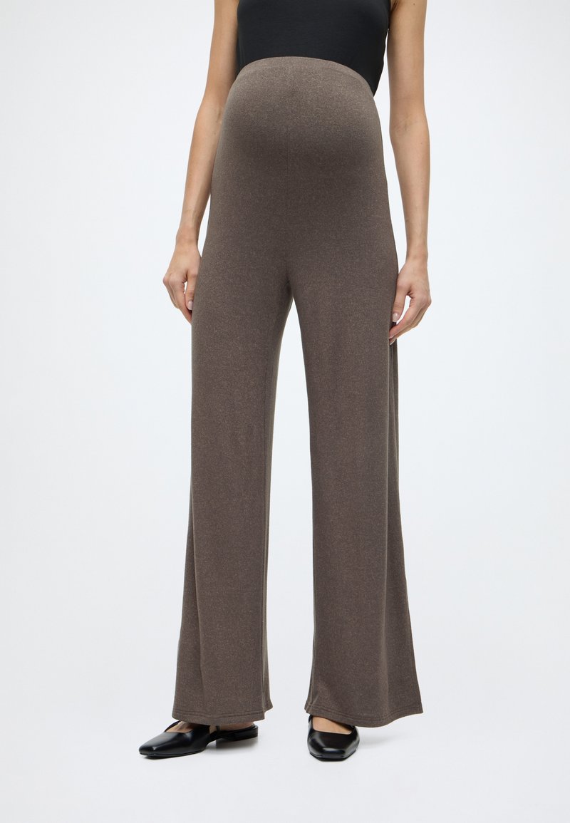 Καφέ παντελόνι με φαρδύ πόδι και υφή, με ψηλή, ελαστική μέση. Φορεμένο με μαύρο τοπ και μαύρα φλατ παπούτσια. Απλός και εφαρμοστός σχεδιασμός.