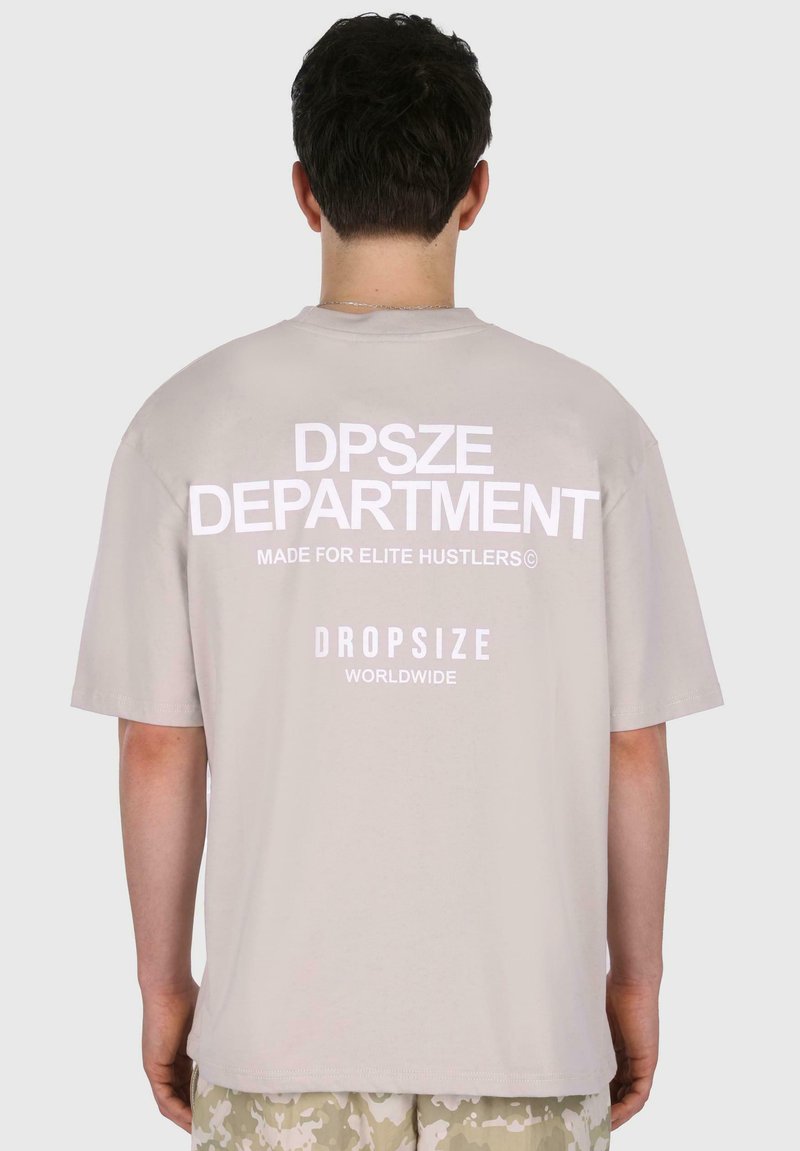 Világosszürke, nagyméretű póló, fehér felirattal a hátsó részén: "DPSZE DEPARTMENT," "MADE FOR ELITE HUSTLERS©," és "DROPSIZE WORLDWIDE."