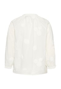 Weiße Baumwollbluse mit rundem Ausschnitt, langen Ärmeln und durchgehend strukturierter Blumenstickerei. Elastische Bündchen an den Ärmelenden.