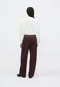 Hvid langærmet top med faldende skuldre, parret med bordeaux vidde bukser med sidelommer og en afslappet pasform.