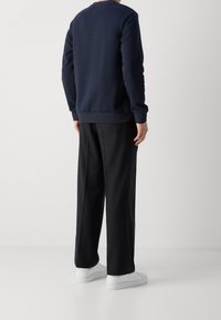 Námořnická mikina s kulatým výstřihem, dlouhými rukávy a žebrovanými manžetami, spárovaná s volnými černými kalhotami a bílými teniskami.