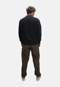 Pullover nero a collo rotondo, pantaloni cargo color khaki con tasche laterali e sneakers bianche. L'outfit presenta una vestibilità comoda e un design semplice.