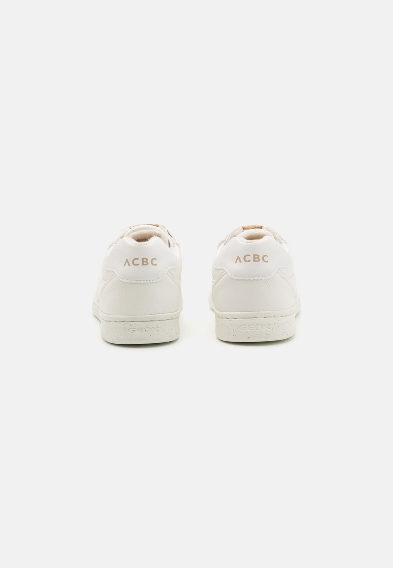 Witte leren sneakers met een gladde textuur, voorzien van een beige accent bij de hiel en gouden branding op de achterkant. Milieuvriendelijk ontwerp.