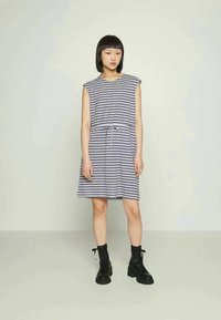 Vestido riscado em azul-marinho e branco, com um design sem mangas, cintura ajustada com cordão. Combinado com botas de combate pretas. Tecido liso e leve.