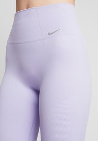 Leggings lavanda a vita alta con texture a costine e logo Nike argento sulla cintura. Tessuto liscio ed elastico.