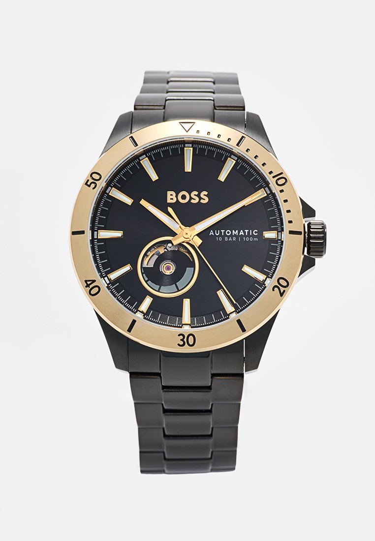 Montre automatique noire avec des accents en or, boîtier rond, cadran noir texturé, marqueurs horaires, et un mouvement visible à travers une découpe.