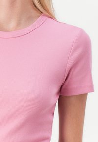 T-shirt rose en jersey côtelé à manches courtes avec un col rond. Le tissu semble doux et extensible, présentant une subtile texture sur toute sa surface.