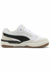 Hvid sneaker med sorte og beige accenter, der har en glat læderoverdel, en tekstureret ruskindsplade og en gummiydersål med vandrette riller.