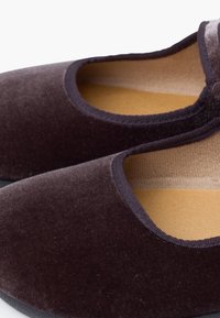 Tmavě hnědé sametové nazouvací boty s hladkým povrchem, zaoblenou špičkou a polstrovanou stélkou. Okraje jsou zakončeny měkkým, elastickým lemováním.
